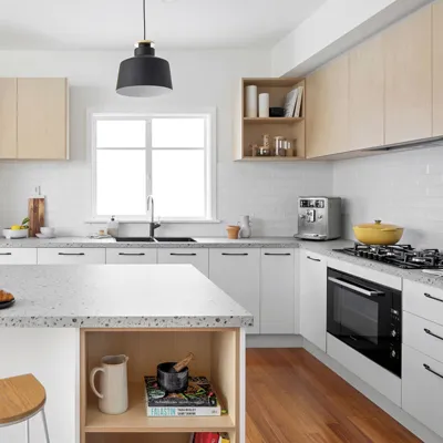 Compact kitchen with white base cabinets, pale wood-tone upper cabinets, a sink under a window and a dark pendant light.