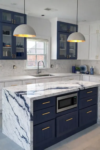 Navy island with a waterfall marble countertop, built-in microwave, glass upper cabinets and dome pendants.