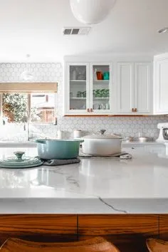 Small image of white kitchen cabinetry, glass-front upper cabinets and a light-colored table in the foreground.